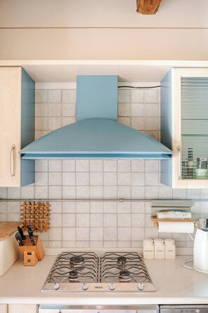 Une cuisine équipée d’une cuisinière à gaz, de meubles de rangement en bois et d’une hotte aspirante bleue.