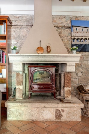 Una chimenea de piedra con una estufa antigua, una estantería a la izquierda y una pared de piedra con un mural.