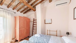 Ein Schlafzimmer mit Holzboden, einem großen Kleiderschrank, einer Hartschiene, einem Bett mit gemusterten Betttextilien und einem kleinen Nachttisch mit Lampe.
