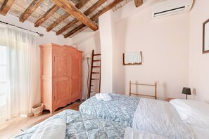 Une chambre avec un plafond en bois, une grande armoire, une échelle, un lit avec une literie à motifs et une petite table de chevet avec une lampe.