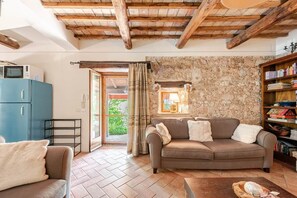 Una sala acogedora con pared de piedra, un sofá, una estantería y techo de madera.