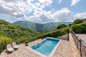 Una piscina con solárium de piedra, rodeada de abundante vegetación y montañas al fondo.