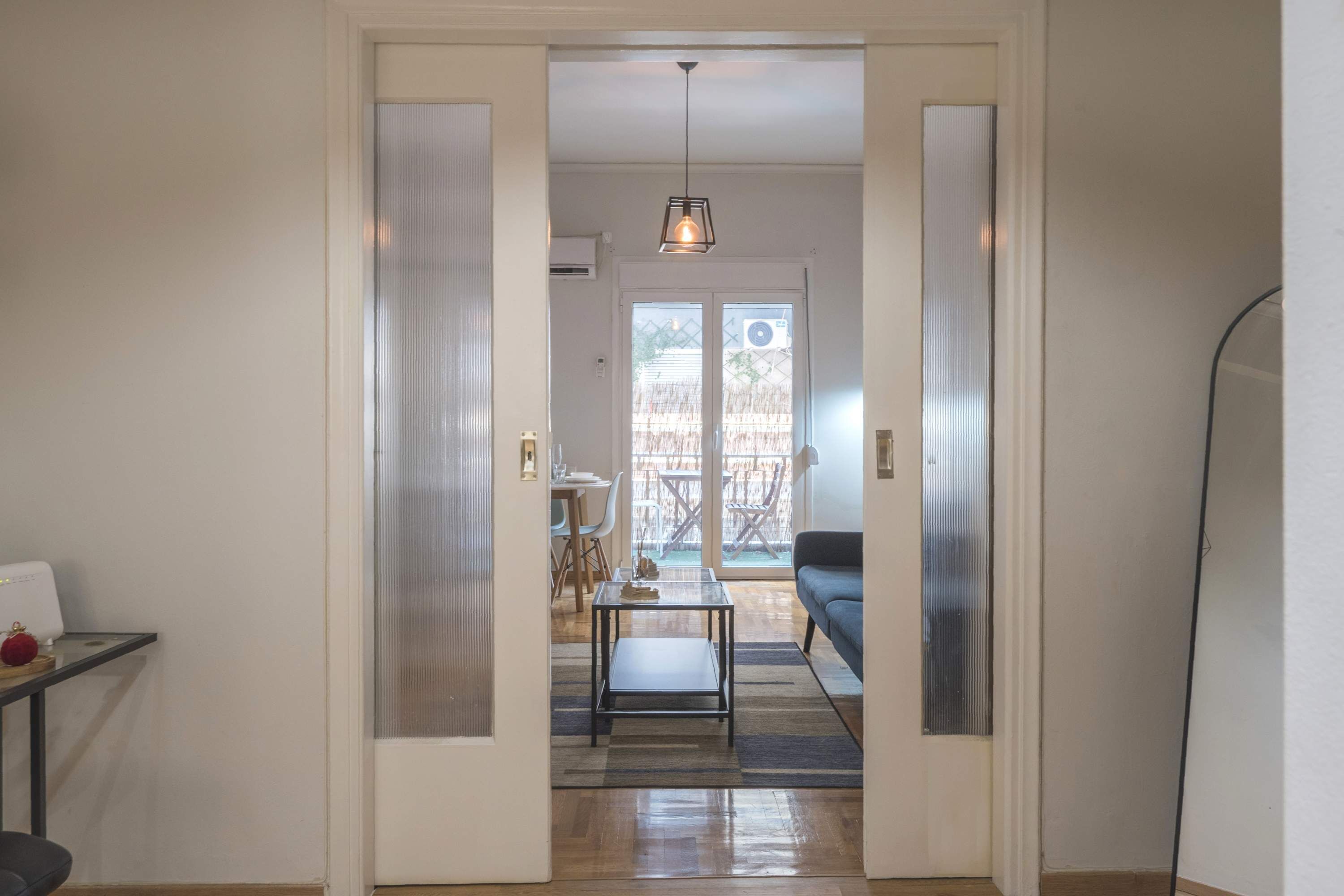 A hallway leading to a dining area with a table and chairs, a sofa, and a hanging light fixture.