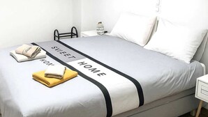Una cama bien tendida con una combinación de colores gris y blanco, una banda decorativa negra y una toalla doblada al lado.