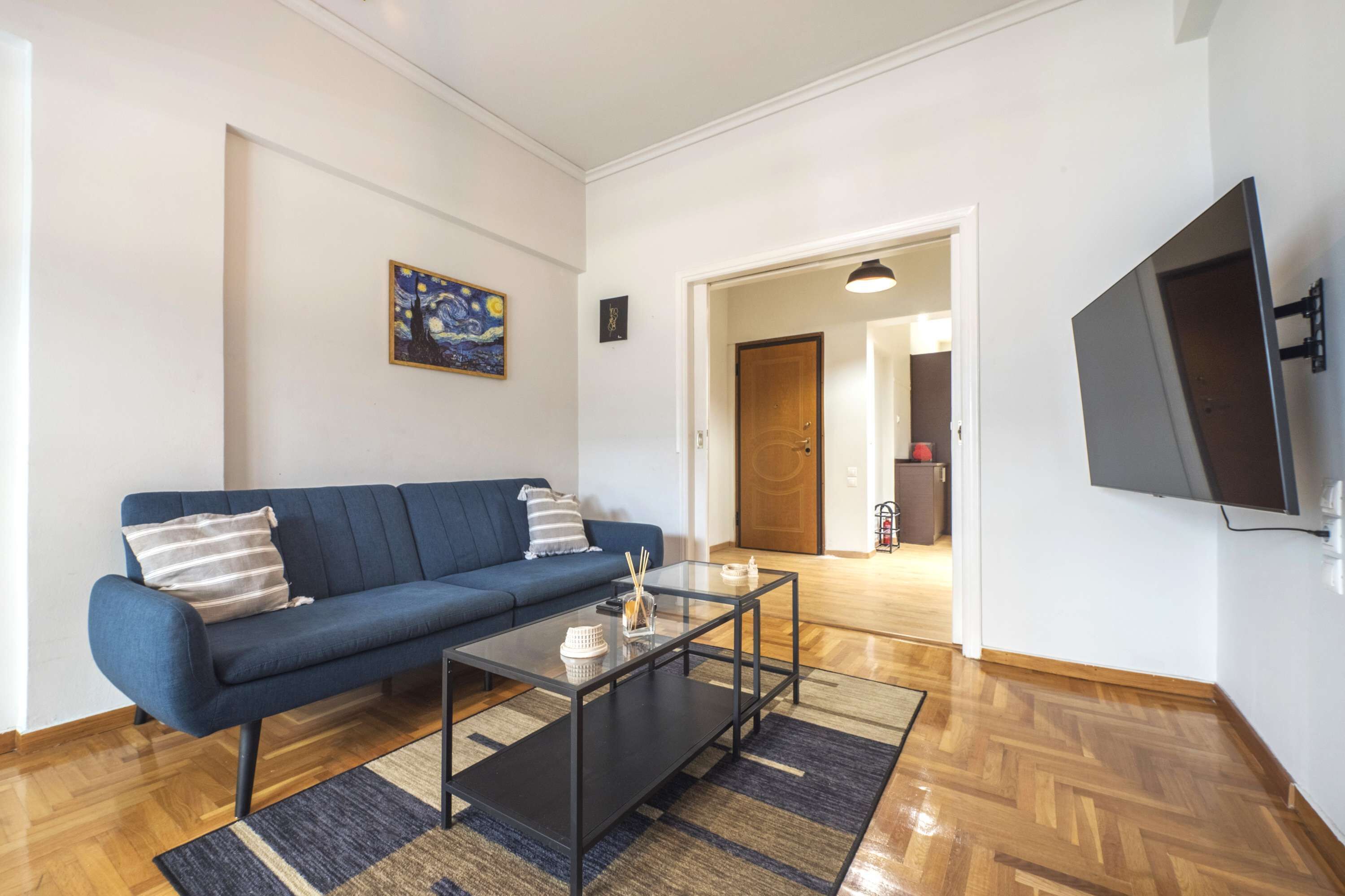 Una sala de estar con un sofá azul, una mesa de centro de vidrio y un cuadro en la pared.
