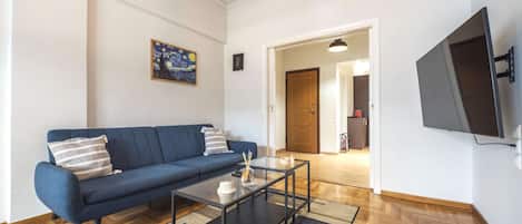 A living room with a blue sofa, a glass coffee table, and a painting on the wall.