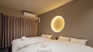 Quarto de hotel com duas camas, ar condicionado na parede e luminária circular.