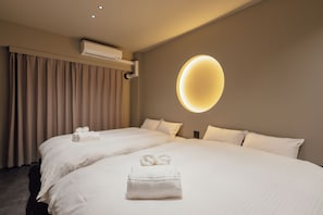 Ein Hotelzimmer mit zwei Betten, einer Wandklimaanlage und einer runden Deckenleuchte.