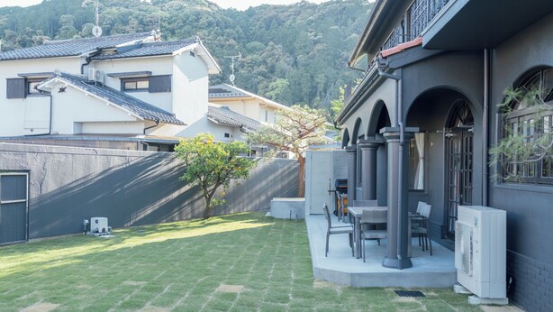 Área residencial com gramado bem cuidado, uma pequena árvore e um pátio com móveis de exterior.