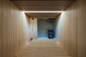 A narrow hallway with wooden walls and a slatted floor leading to a room with a fireplace.