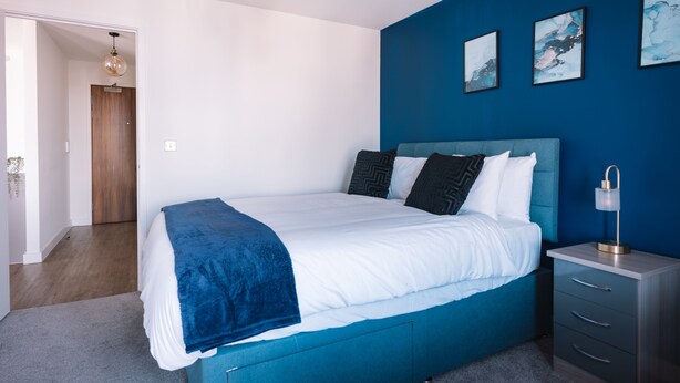 Quarto com cama, mesa de cabeceira, cômoda e porta que dá para outro aposento.