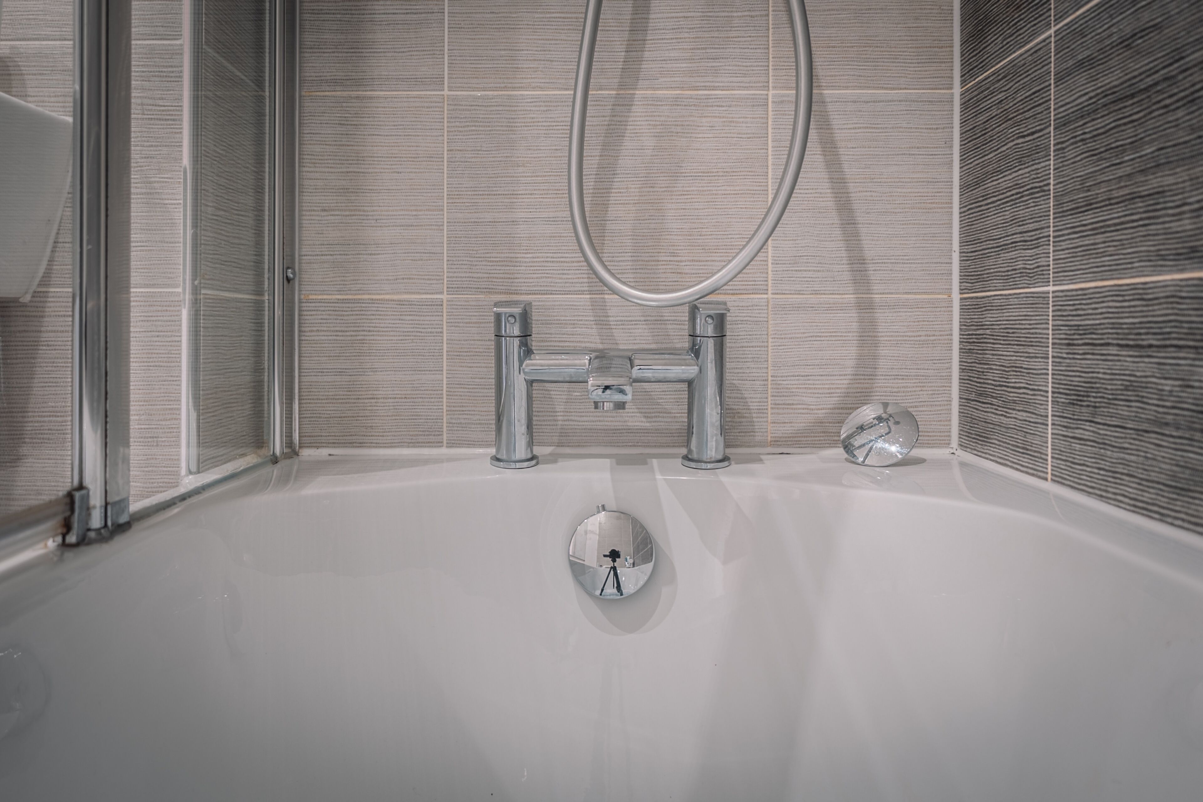 Une salle de bain moderne avec une baignoire, une douchette à main et un miroir fixé au mur.