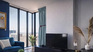 Uma sala de estar moderna com uma janela ampla, televisão de tela plana, sofá azul e plantas decorativas.