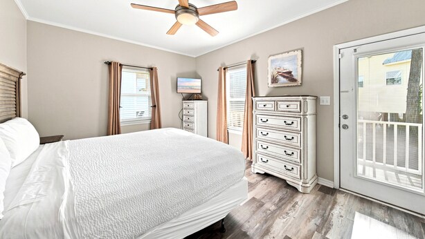 Une chambre à coucher comprenant un lit, une commode, un ventilateur de plafond et une porte donnant sur l’extérieur.