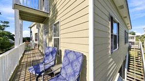 Une maison à deux étages avec un balcon, deux chaises bleues à motifs et une balustrade blanche.