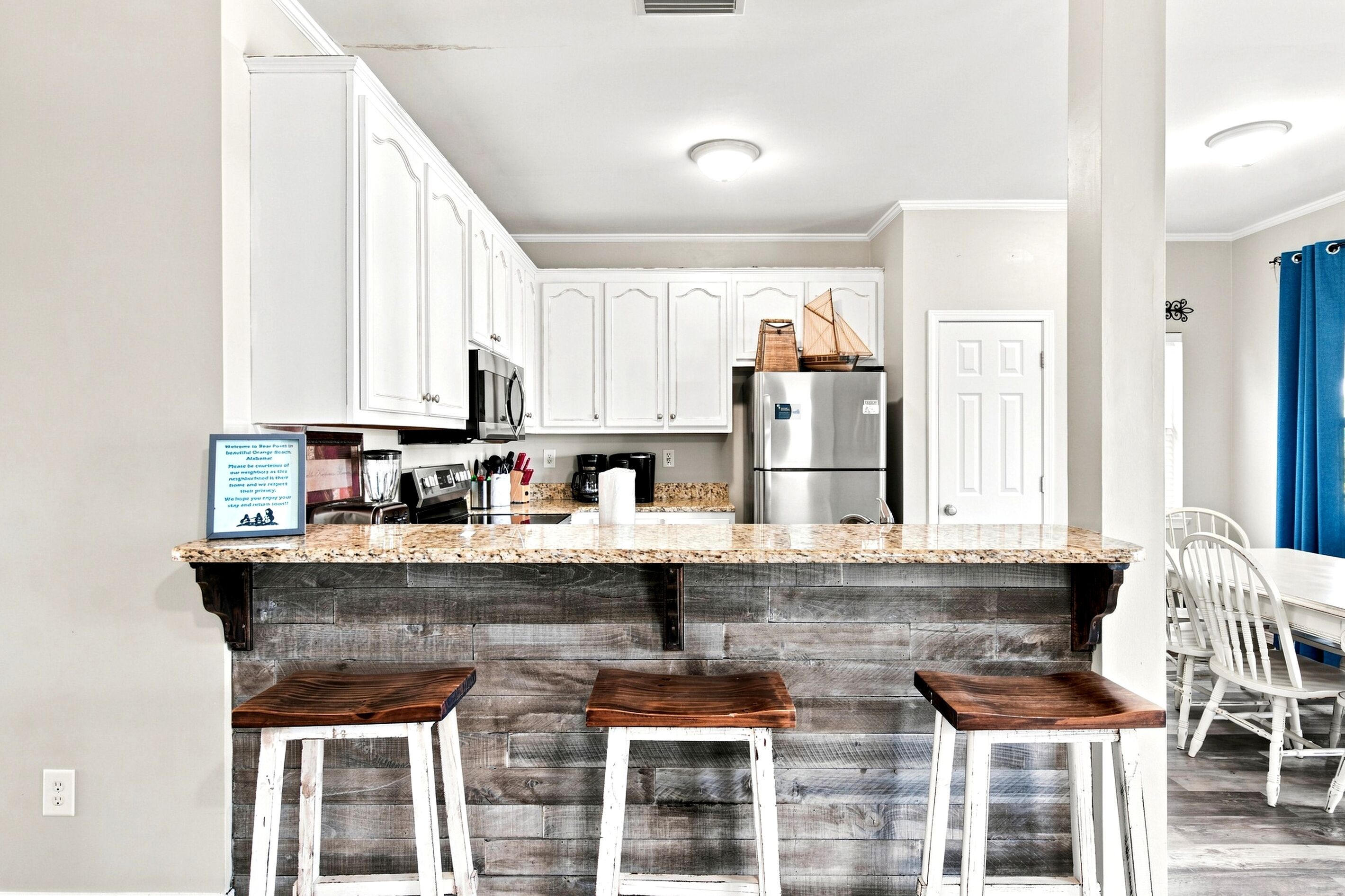 A kitchen with white cabinets, a stainless steel refrigerator, a granite countertop, and a wooden island with stools.