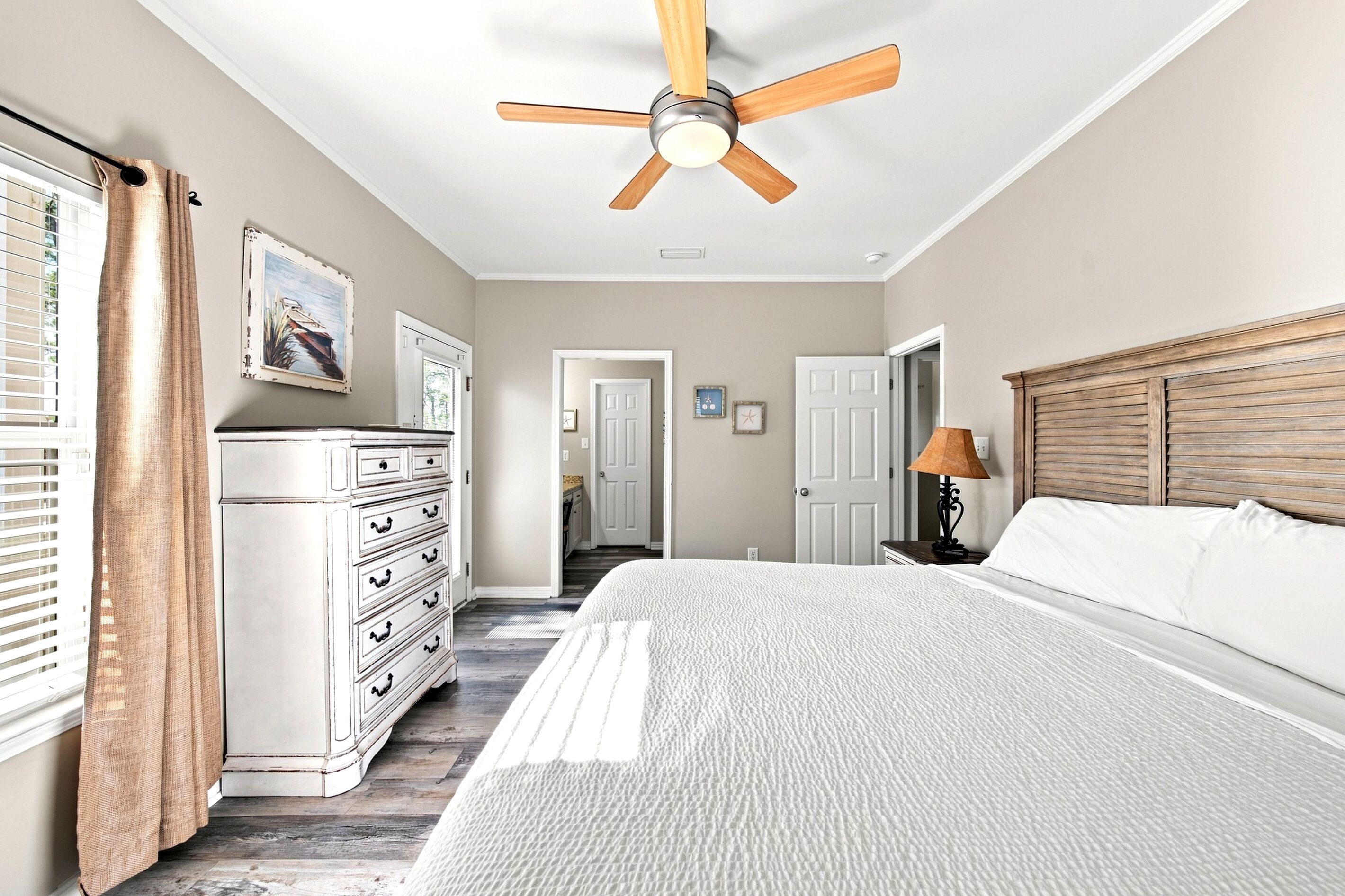 A bedroom with a bed, a dresser, a ceiling fan, and a door leading to another room.