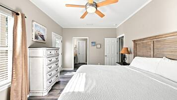 A bedroom with a bed, a dresser, a ceiling fan, and a door leading to another room.