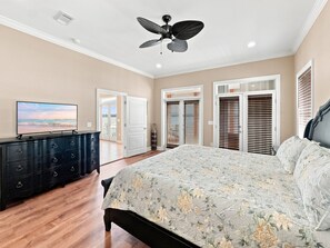 Une chambre à coucher avec un lit, une commode, un ventilateur de plafond et un téléviseur posé sur la commode.