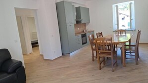 Eine moderne Küche mit grauen Schränken, einem Esstisch mit Holzstühlen und einem Fenster, das für natürliches Licht sorgt.