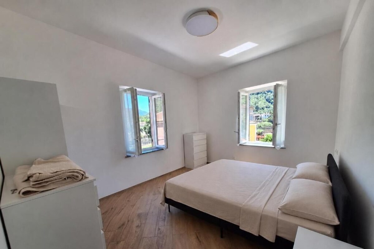 A bedroom with a bed, two windows, a ceiling light, and a wooden floor.