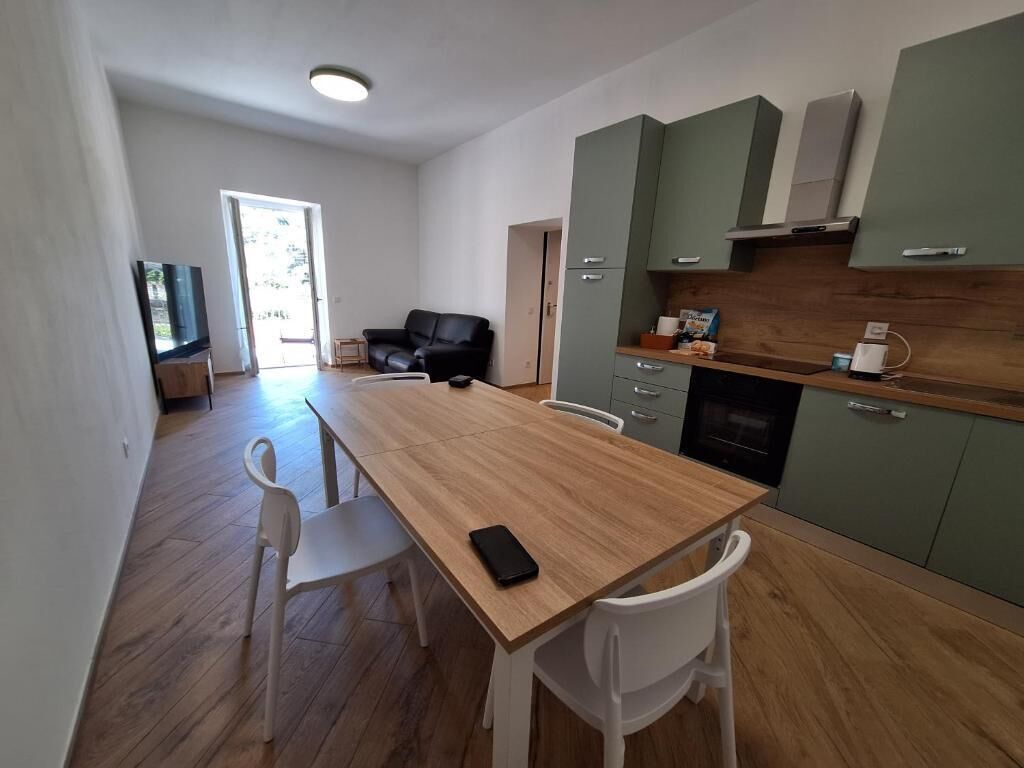Eine moderne Küche mit einem Holztisch, weißen Stühlen, einem Fernseher und einem grünen Schrank.
