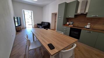 Eine moderne Küche mit einem Holztisch, weißen Stühlen, einem Fernseher und einem grünen Schrank.