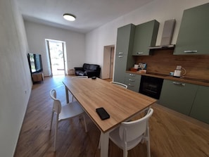 A modern kitchen with a wooden table and white chairs, a television, and a green cabinet.