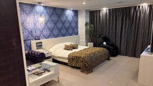 A modern bedroom with a bed, a massage chair, a glass coffee table, and a wall with a blue patterned design.