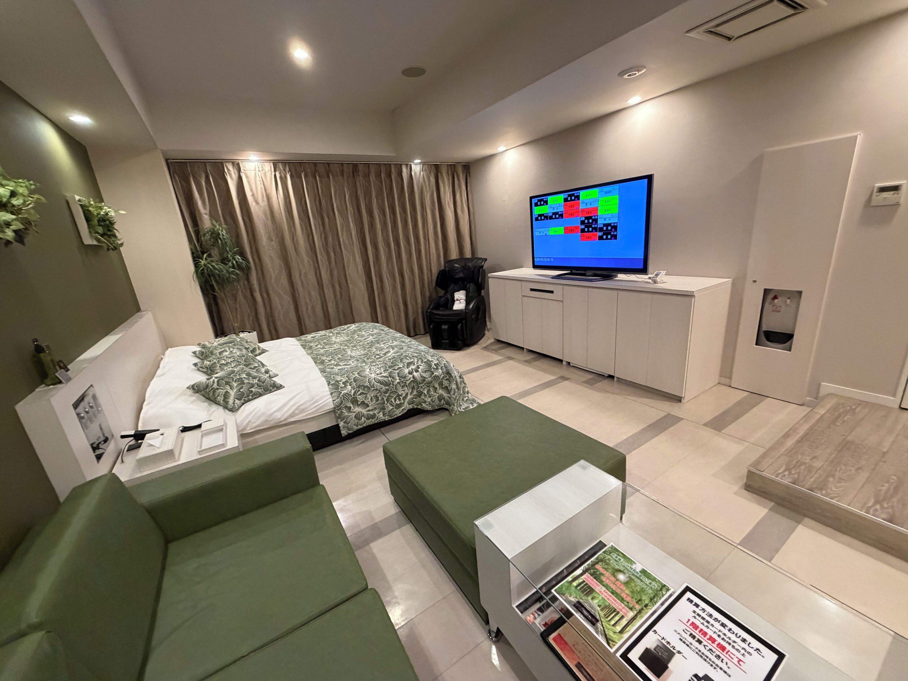 Une chambre d’hôtel avec un lit, un canapé vert, un téléviseur fixé au mur, une armoire et une petite table sur laquelle sont posées des brochures.