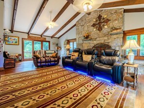 A spacious living room with leather sofas, a patterned rug, stone wall, and a fireplace. - Beautiful Home on a Mountainous Tree Farm (Newland)