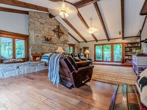 A spacious living room with a stone fireplace, leather recliner, and a large bookshelf. - Beautiful Home on a Mountainous Tree Farm (Newland)
