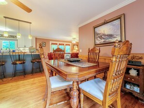 A dining area with a wooden table and chairs, a kitchen in the background, and a painting on the wall. - Beautiful Home on a Mountainous Tree Farm (Newland)