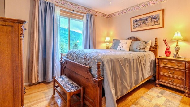 Een slaapkamer met een houten bed, een bankje, een nachtkastje en een raam met gordijnen.