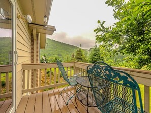 A wooden deck with a metal table and chairs, overlooking a lush green landscape. - Beautiful Home on a Mountainous Tree Farm (Newland)