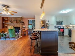 A spacious kitchen with a central island, bar stools, and a fireplace. - Beautiful Home on a Mountainous Tree Farm (Newland)