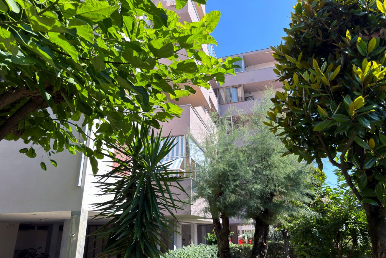 A multi-story building with balconies, surrounded by lush greenery and trees.