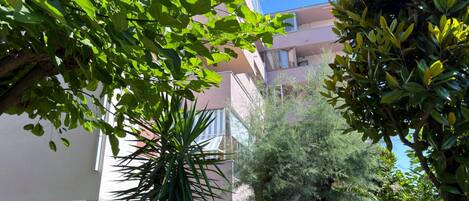 A multi-story building with balconies, surrounded by lush greenery and trees.