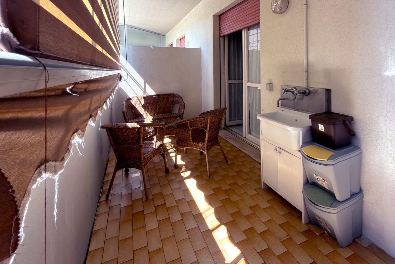 A small balcony with wicker furniture, a sink, and storage boxes.