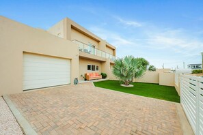 A modern two-story house with a garage, a small outdoor seating area, and a well-maintained lawn. - Modern Two Villas • 6BR • 2 Private Pools • Aruba Escape (Noord)