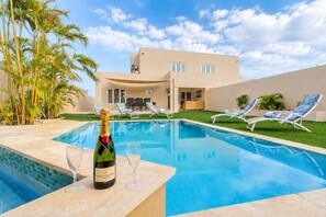 A swimming pool with lounge chairs, a bottle of champagne, and a glass on the edge. - Modern Two Villas • 6BR • 2 Private Pools • Aruba Escape (Noord)