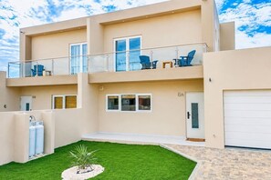 A two-story building with a balcony, a garage, and a small lawn area. - Modern Two Villas • 6BR • 2 Private Pools • Aruba Escape (Noord)