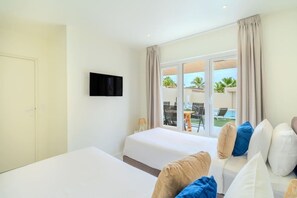 Ein Hotelzimmer mit zwei Betten, einem Fernseher und Blick auf einen Pool und Sitzgelegenheiten im Freien.