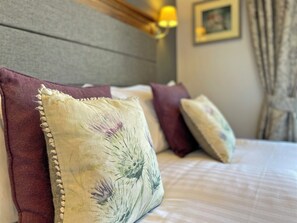 A bed with multiple pillows, a headboard, and a wall-mounted lamp. - Brookhouse Mill (Denbigh)
