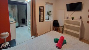 A hotel room with a bed, a TV mounted on the wall, a desk with a chair, a potted plant, and a sliding door leading to a bathroom. - Roubaix Downtown Studio: Fast WiFi & Workspace (Roubaix)