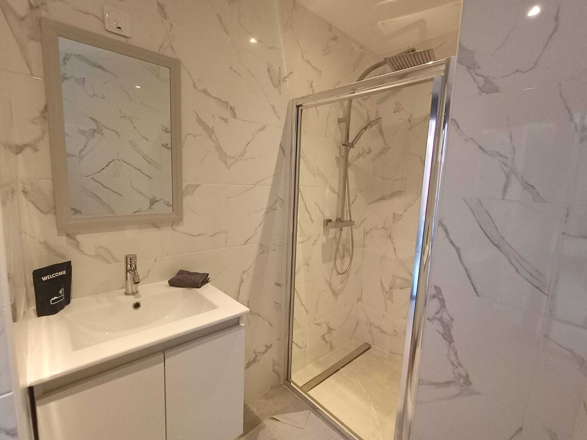 Ein Badezimmer mit Marmorwand, Waschbecken, Spiegel und einer Duschkabine aus Glas.