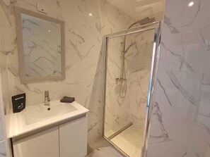 A bathroom with a marble wall, a sink, a mirror, and a glass shower enclosure.