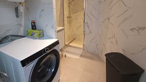 A compact laundry area with a washing machine, a drying rack, and a shower enclosure. - Roubaix Downtown Studio: Fast WiFi & Workspace (Roubaix)