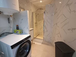 A compact laundry area with a washing machine, a drying rack, and a shower enclosure. - Roubaix Downtown Studio: Fast WiFi & Workspace (Roubaix)