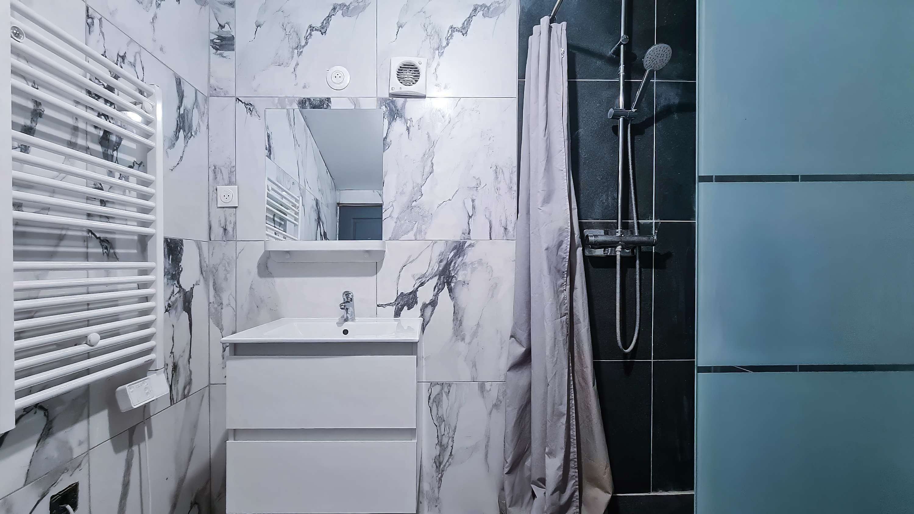 A bathroom with a white sink, a mirror, a shower with a handheld showerhead, and a towel rack.